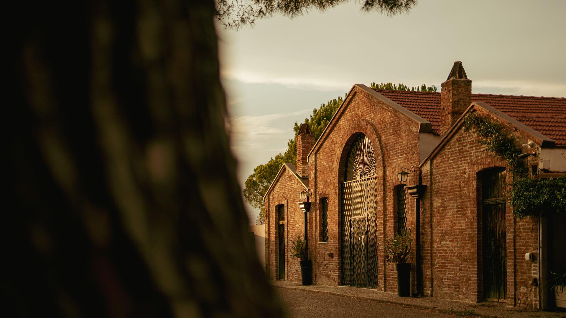 Edificio in mattoni con portone in ferro, al tramonto, circondato da alberi.