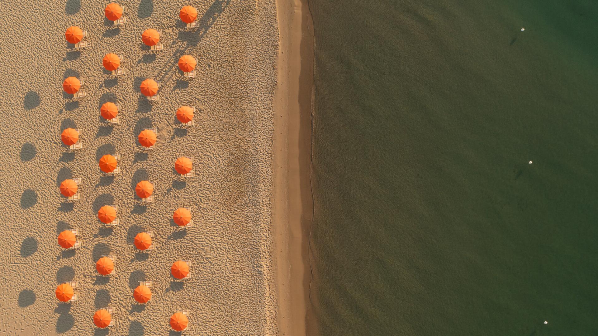 Coppia che si gode un pranzo in spiaggia con vino, sotto ombrelloni arancioni.