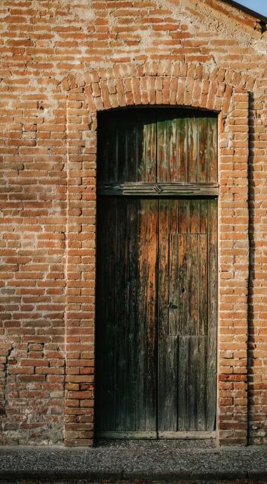 Porta di legno antica incorniciata da mattoni rossi su edificio rustico.