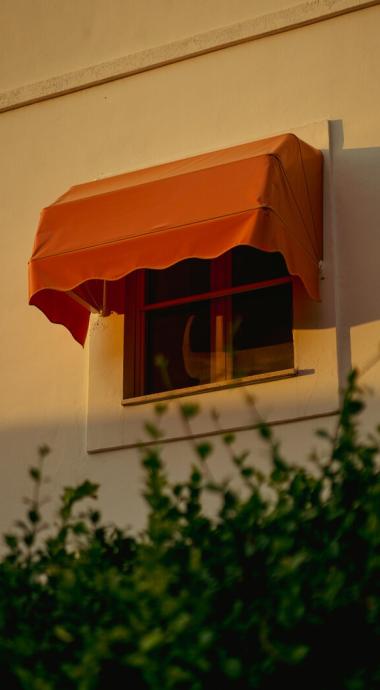 Finestra con tenda arancione su un edificio, circondata da foglie verdi.