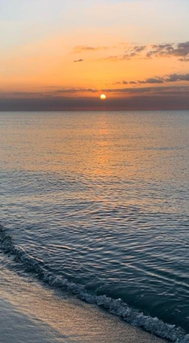 Tramonto sul mare con onde leggere e cielo arancione.