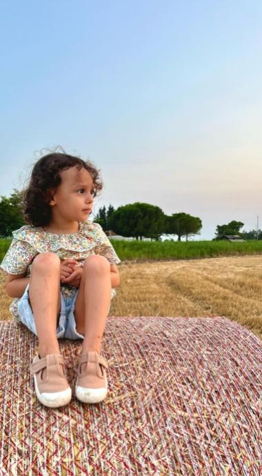 Bambina seduta su una balla di fieno in un campo al tramonto.