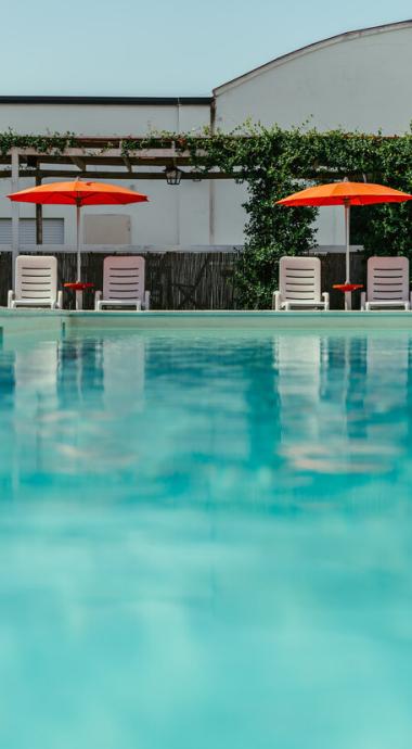 Piscina con lettini e ombrelloni arancioni, atmosfera estiva e rilassante.