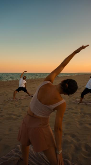 Gruppo di persone fa yoga sulla spiaggia al tramonto.