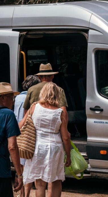 Persone salgono su un minibus con borse e cappelli.