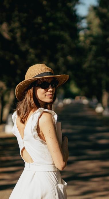 Donna con cappello di paglia e occhiali da sole su un sentiero alberato.