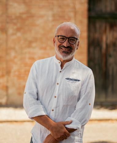 Uomo sorridente con camicia bianca e occhiali, sfondo di mattoni.