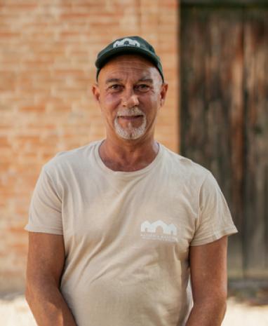 Uomo con cappello e maglietta beige, sfondo di mattoni e porta di legno.