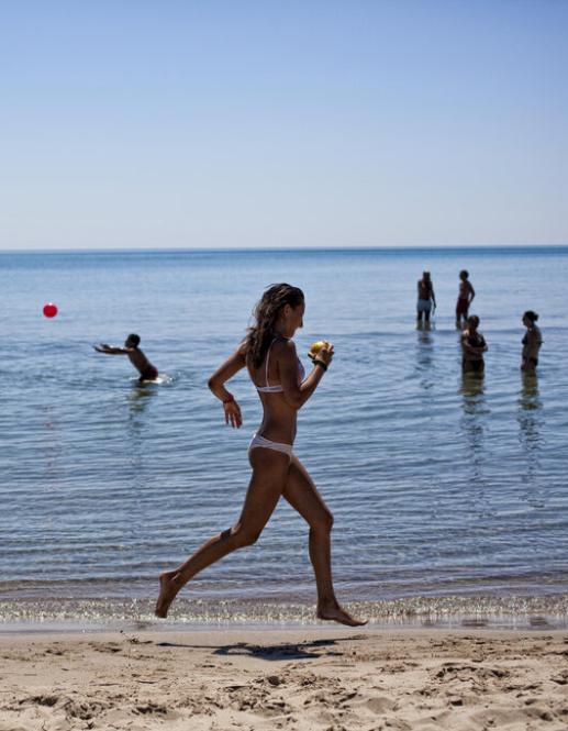 Spiaggia con ombrelloni arancioni, sabbia chiara e mare calmo, due persone passeggiano.