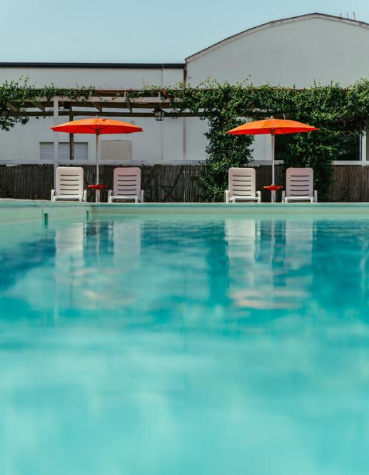 Piscina all'aperto con lettini e ombrelloni arancioni, circondata da un prato verde.