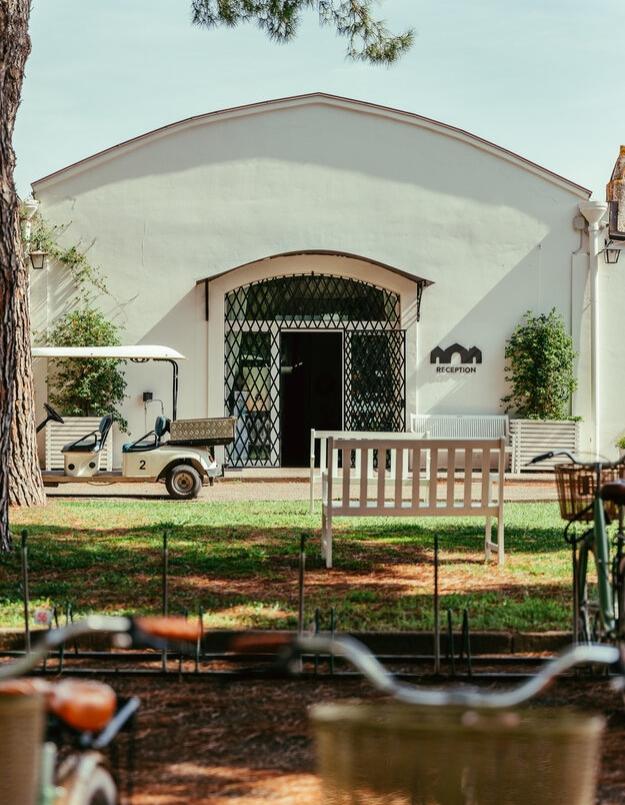 Edificio bianco con reception, golf cart e biciclette parcheggiate sul prato.