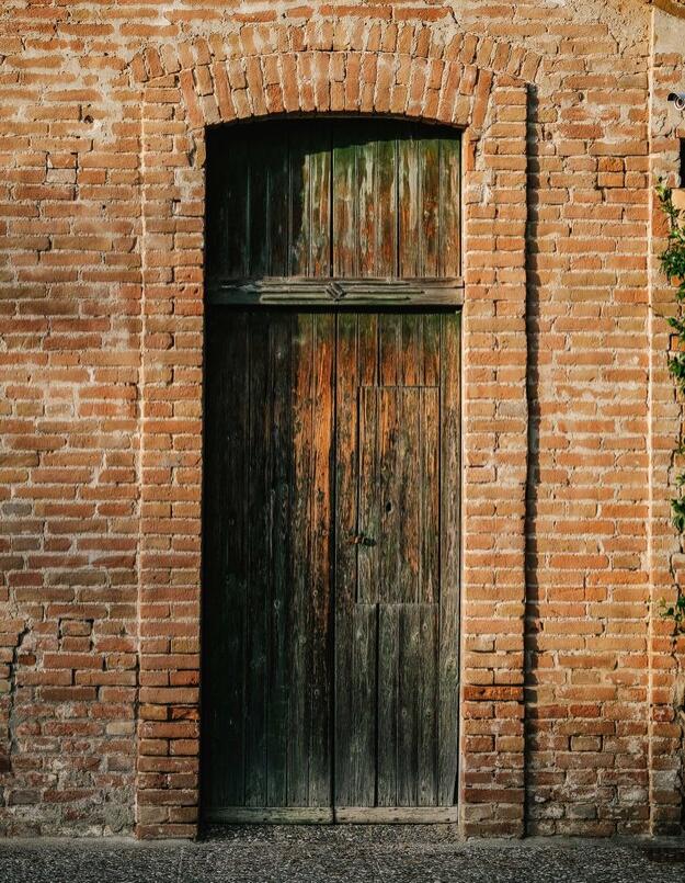 Porta di legno antica incorniciata da mattoni rossi su edificio rustico.