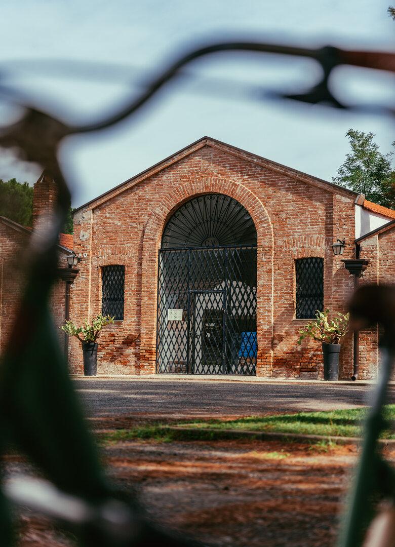 Edificio in mattoni con portone in ferro, circondato da piante in vasi.