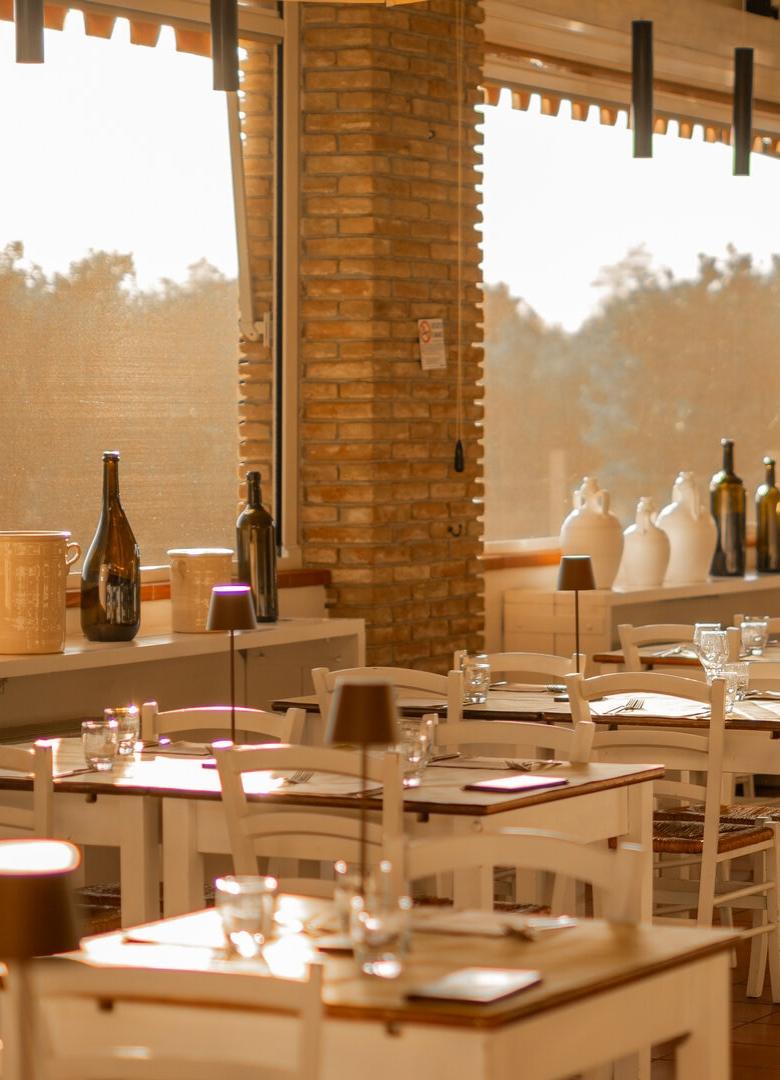 Ristorante accogliente con tavoli apparecchiati, mattoni a vista e ampie finestre luminose.