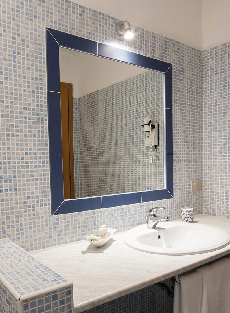 Bagno con piastrelle blu, specchio grande e asciugacapelli a parete.