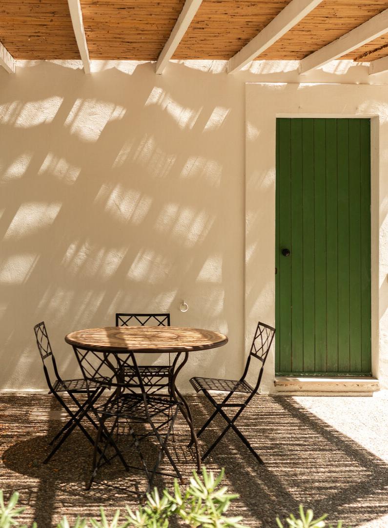 Terrazza con tavolo e sedie, ombra di pergola, porta verde, atmosfera mediterranea.