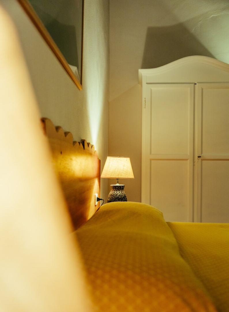 Camera da letto con lampada accesa, letto giallo e armadio bianco.