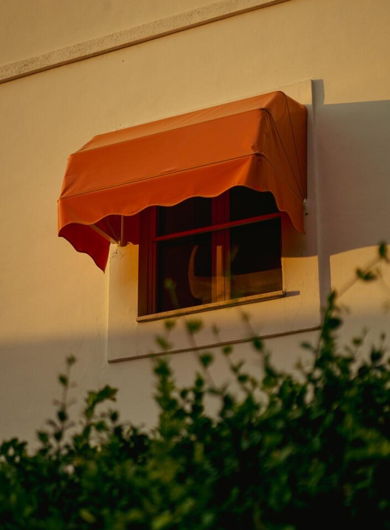 Finestra con tenda arancione su un edificio, circondata da foglie verdi.