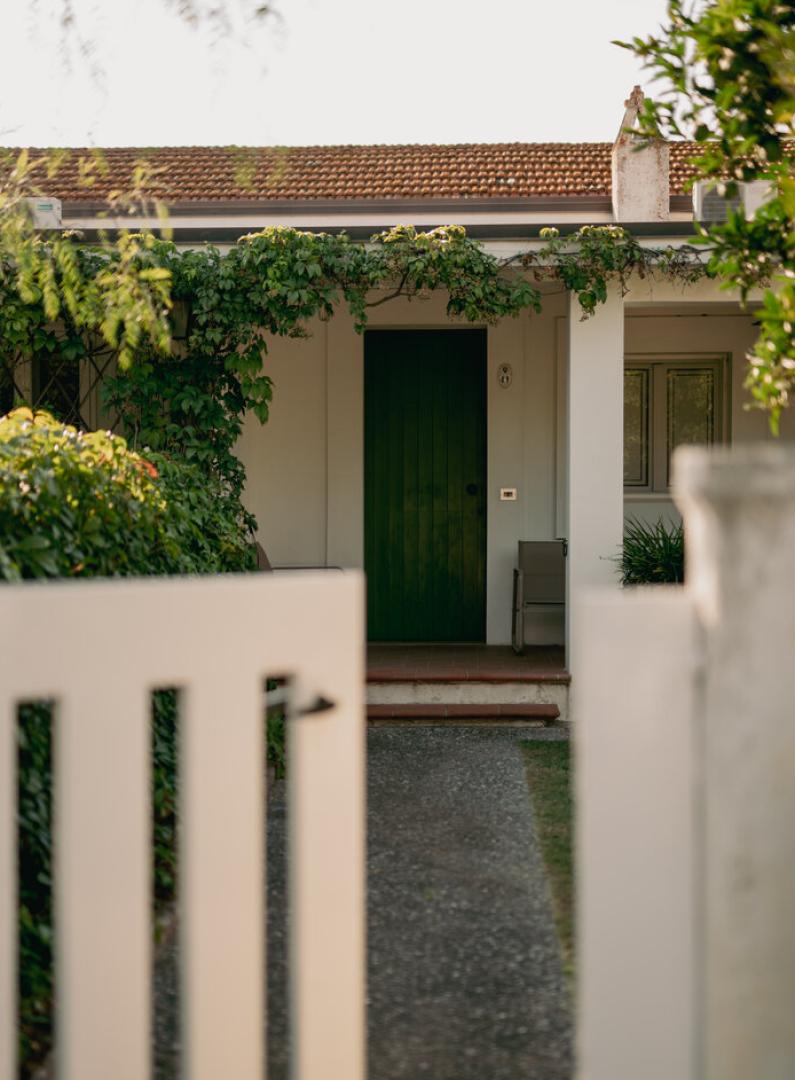 Ingresso di una casa con porta verde e piante rampicanti, visto attraverso un cancello.